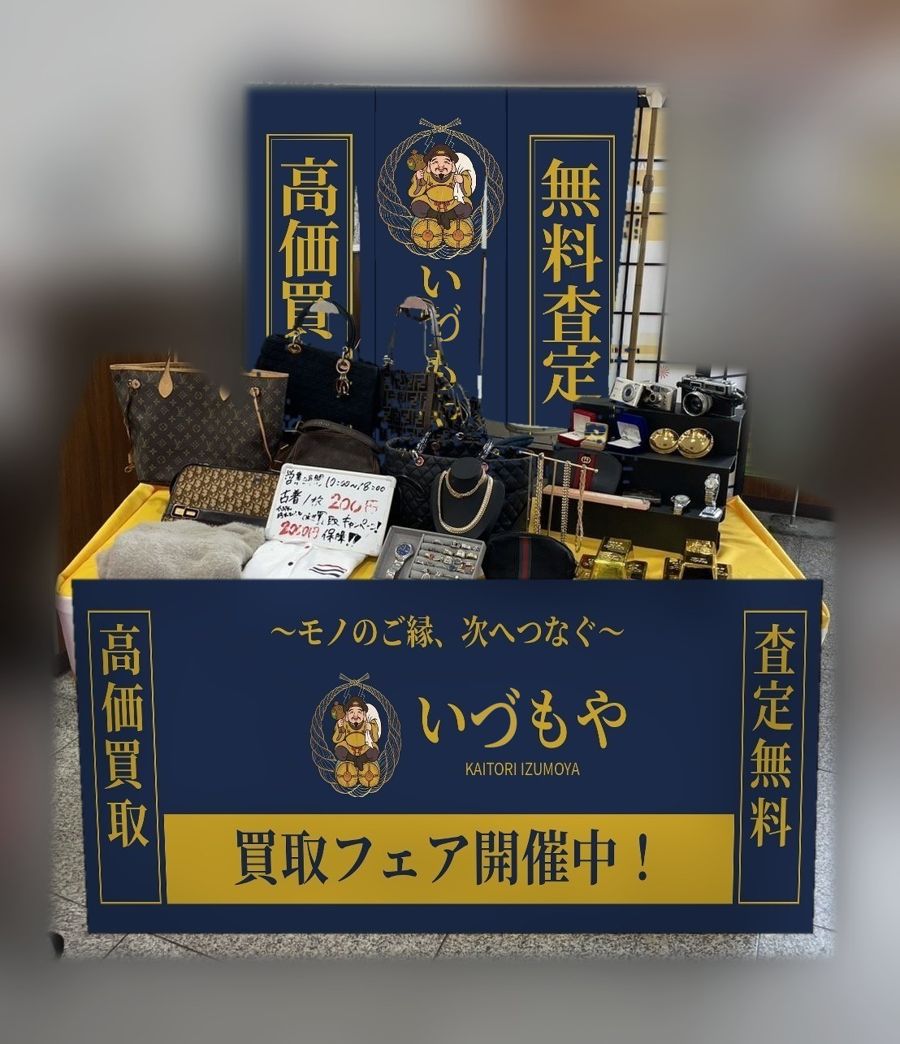 商業施設の催事場に設けたいずもやの買取ブース。紺地に金文字ののれんと巻き幕、黄色のクロスを掛けた陳列机